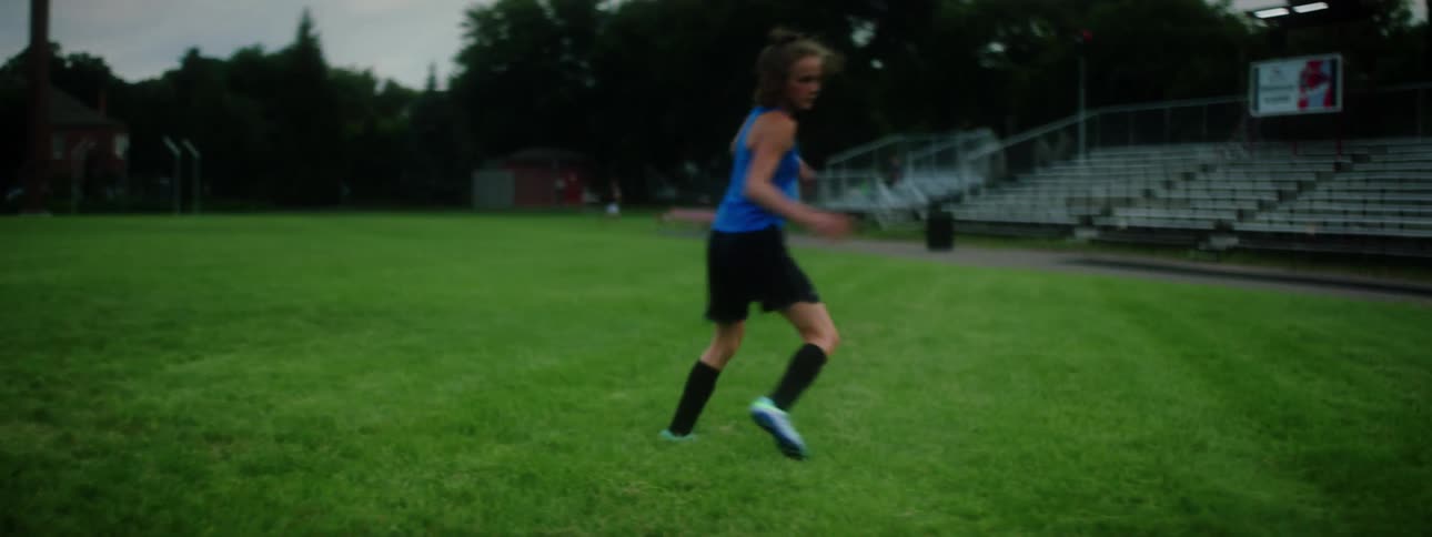 A woman in a soccer field kicking a soccer ball