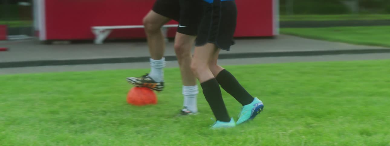 A soccer player defending an orange soccer ball from another player trying to steal it