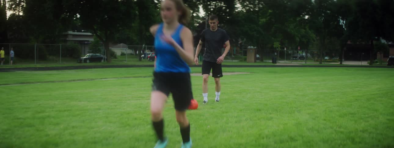 A man kicks the soccer ball to a running female