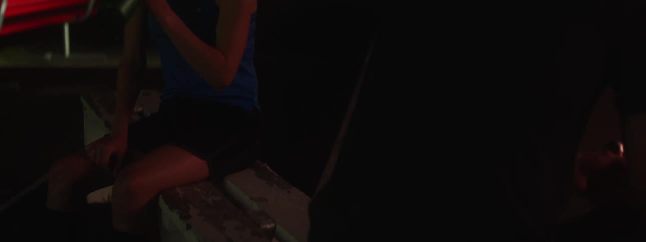 A girl sitting on a bench at the field at night drinks from a gatorade bottle