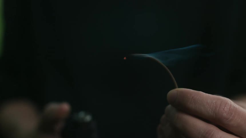 A white uses a lighter to set fire to a piece of incense