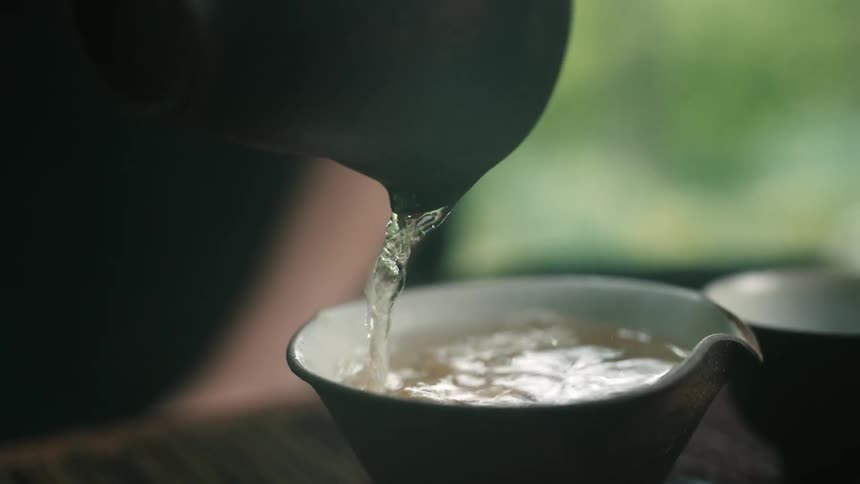 Steaming hot tea is poured into a teacup