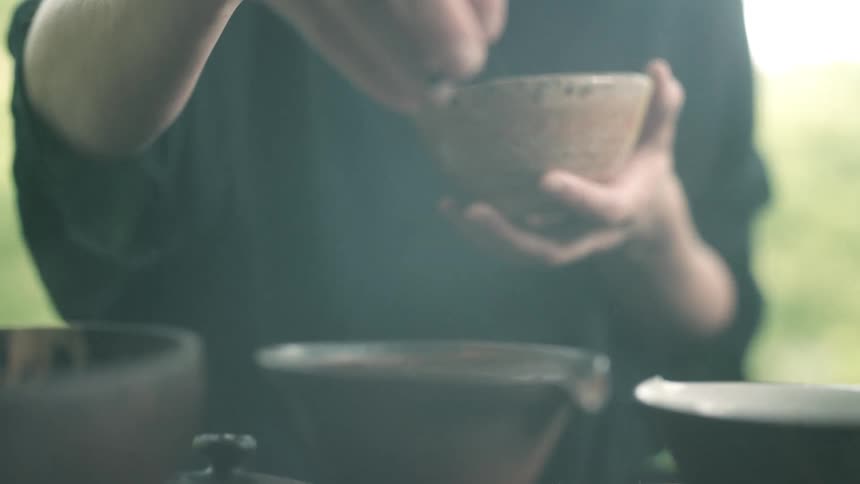 A white woman sits in an open home and sprinkles seasoning from one bowl to another