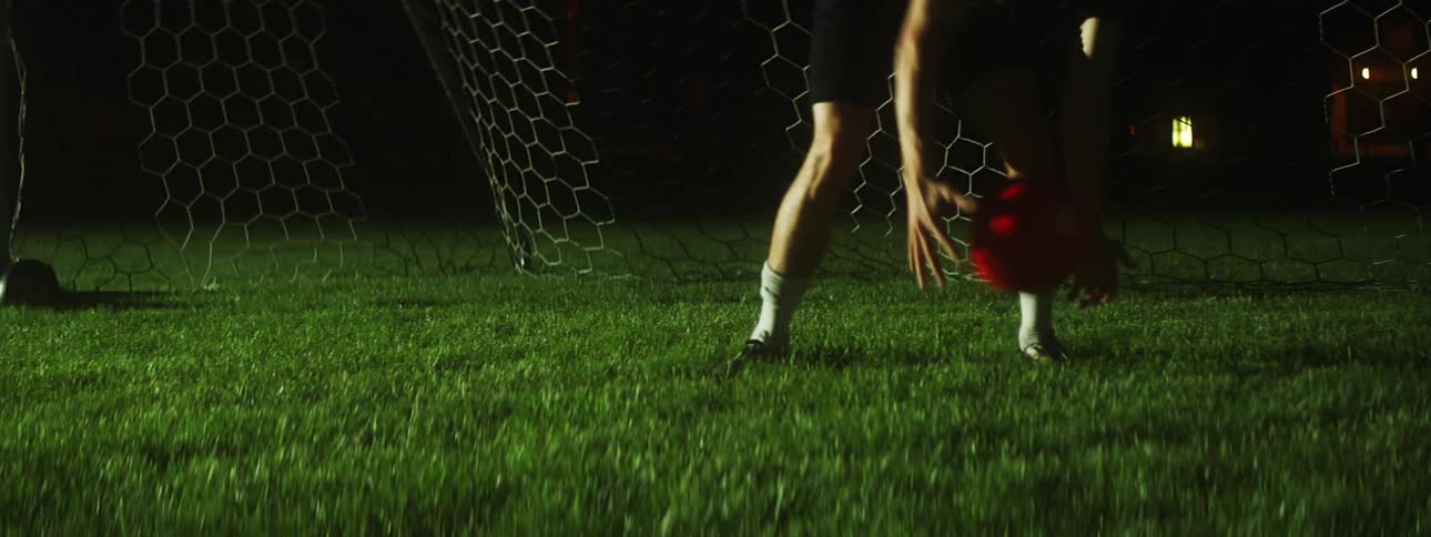 Soccer goalie blocks and returns ball on field at night