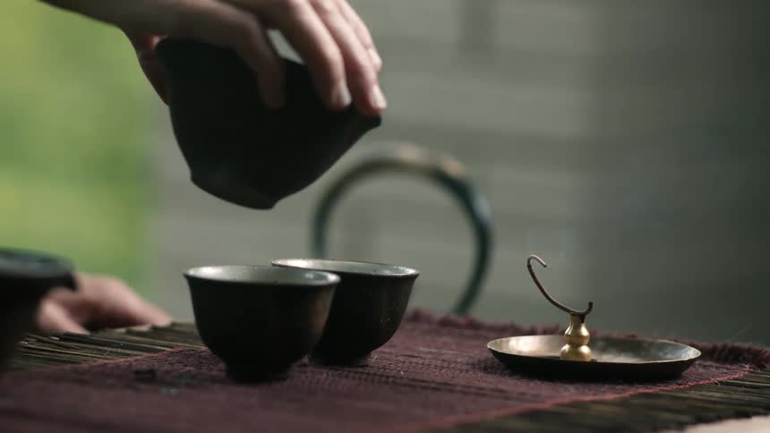 Steaming hot tea is poured into teacups next to burning incense