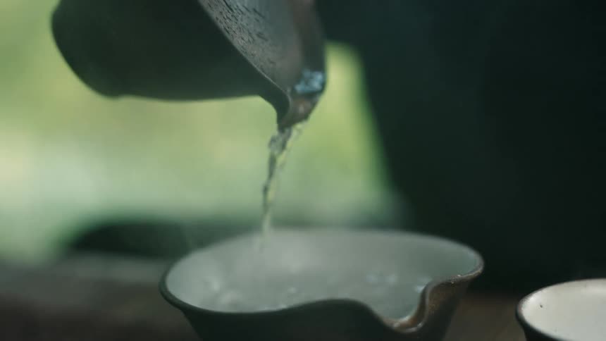 Person pours steaming water from tiny stoneware pot into small bowl
