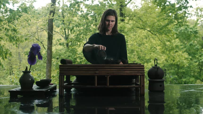 A woman in front of a forest pours water in to bowls