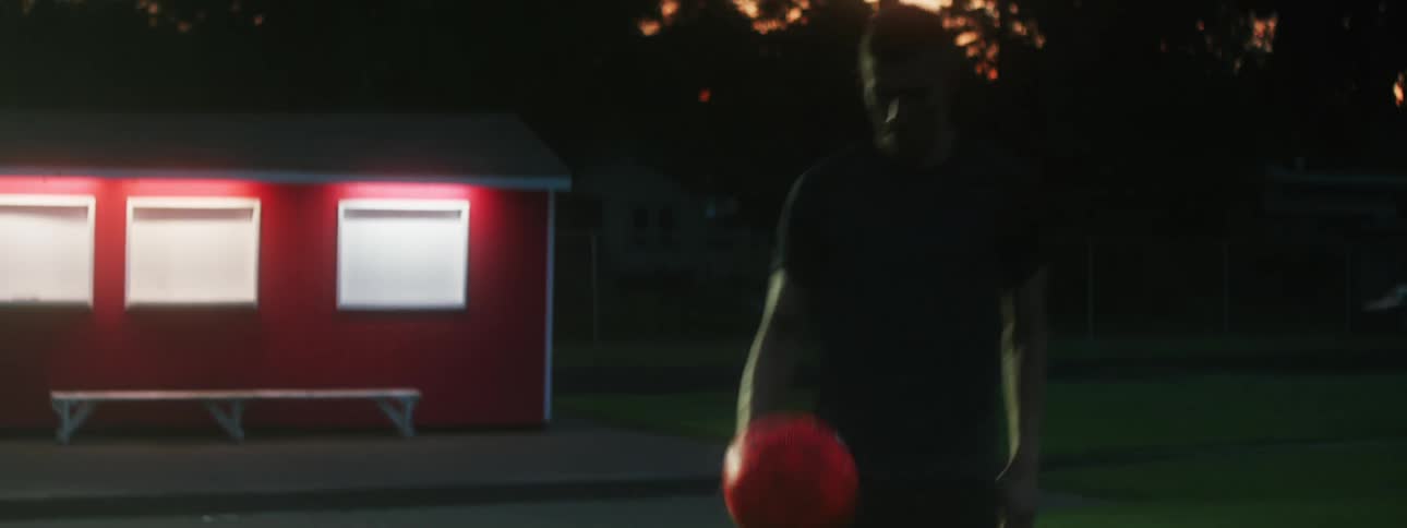 A young girl flips over a ball picks it up and tosses it to a boy