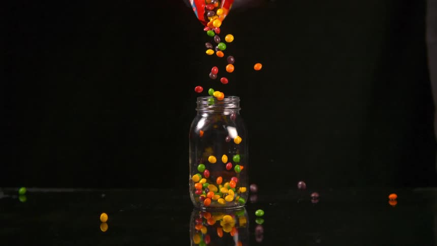 A bag of skittles being poured into a glass mason jar
