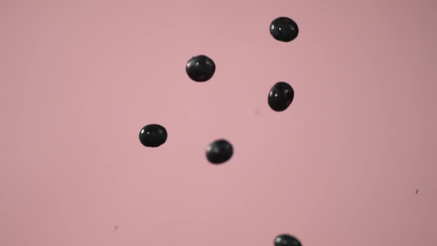 Blueberries fall down against a pink wall