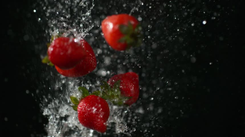 Strawberries and water spray in front of black background