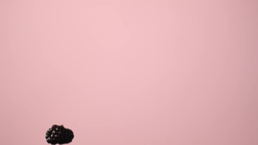 Blackberries and raspberries falling against pink background