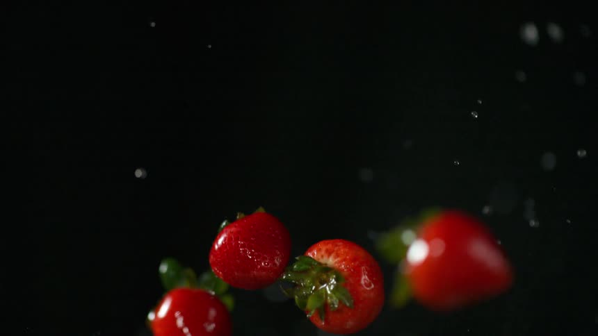 Water droplets being flung from spinning strawberries as they fall through a dark room