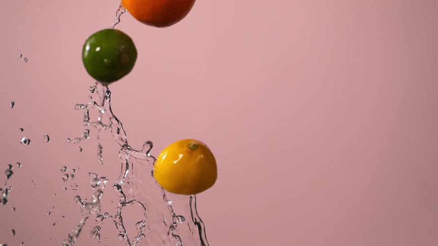 Citrus fruits and water fly through the air in front of a pink background