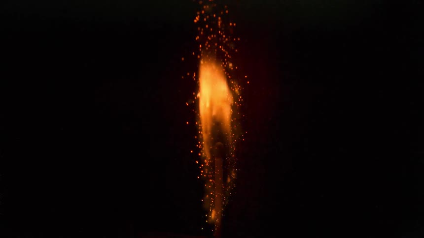 Slow motion shot of match igniting in flames in a dark room