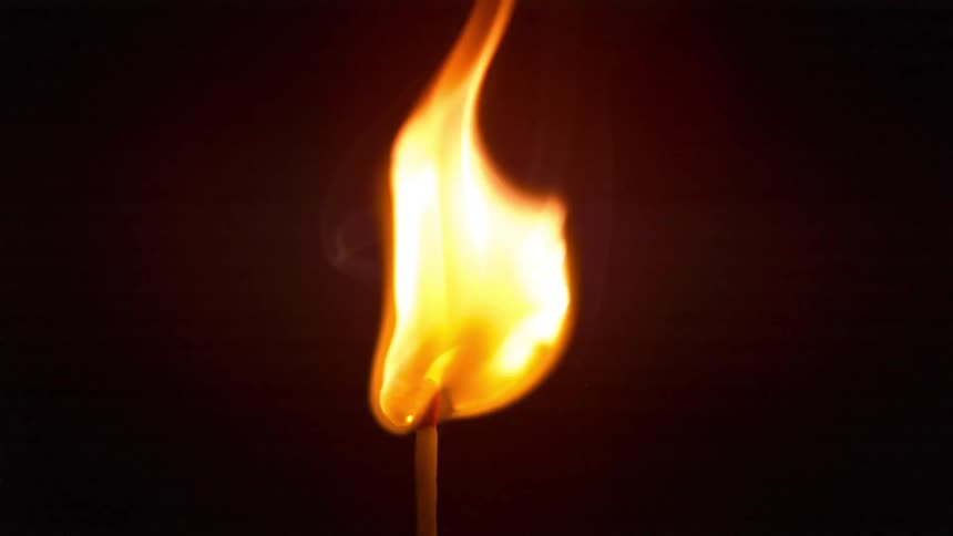 A flame burning on the head of a match in a dark room