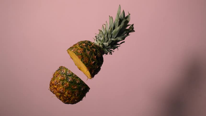 Pineapple cut in half falls in slow motion against pink background