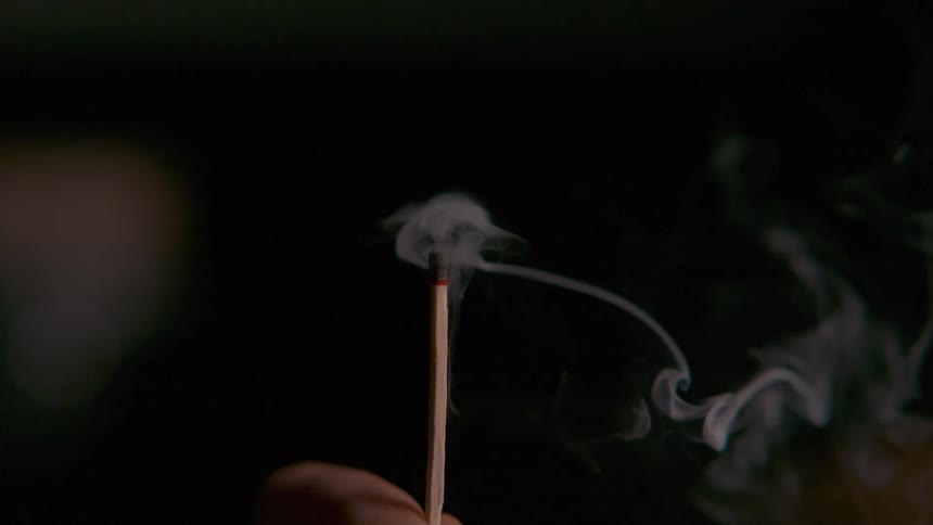 Smoke swirls around a burning matchstick