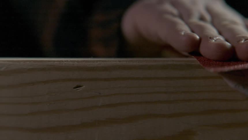 A man uses sandpaper to smooth the end of a piece of a wood