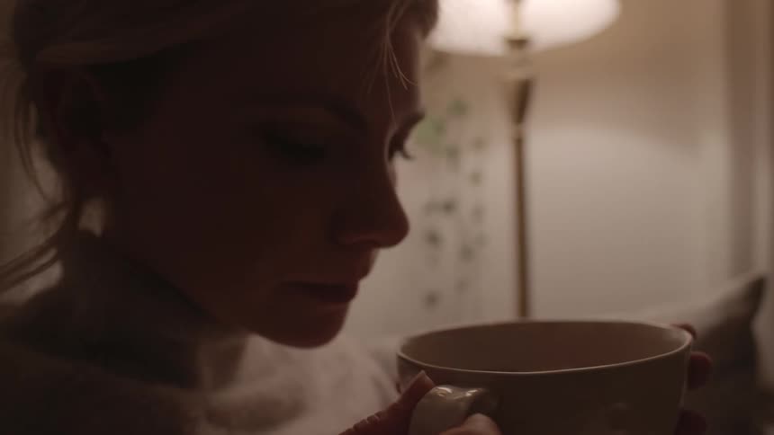 A woman sitting in her living room sipping a hot drink and relaxing