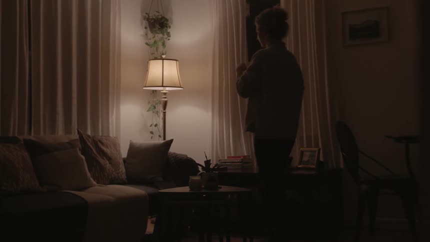 A woman walks in to her living room and sits down and takes a drink of her tea