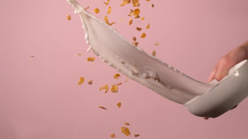 A person tosses a bowl of milk into a stream of falling cereal bits