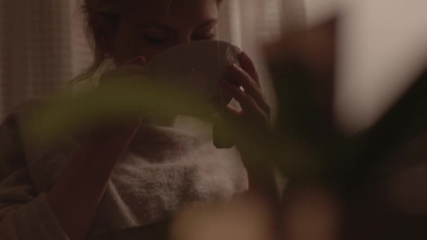 Female sitting at home alone sips on a cup of tea with a sad look on her face