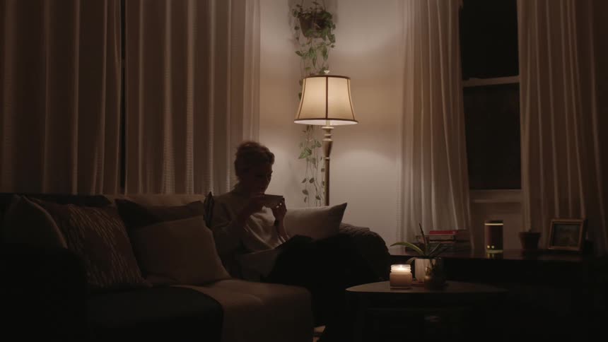 Silhouette of woman relaxing drinking tea by candle light at night in living room