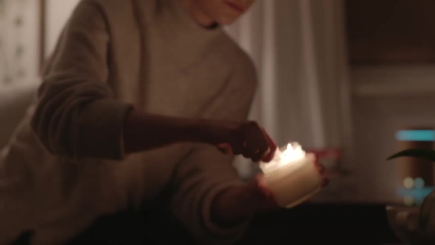 A white woman lights a candle in a home at night