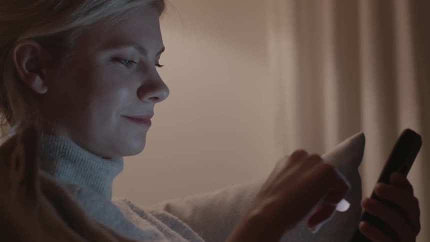 A woman sits in a dimly lit room with her cell phone