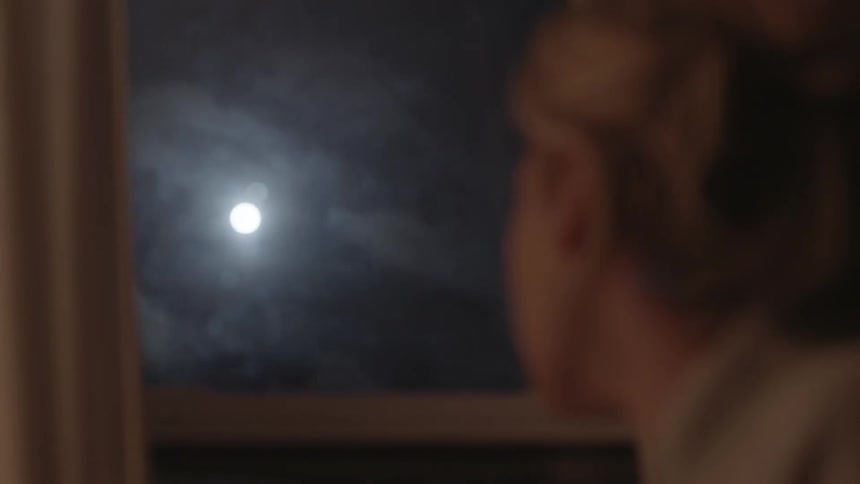 A woman looks out a window at the moon