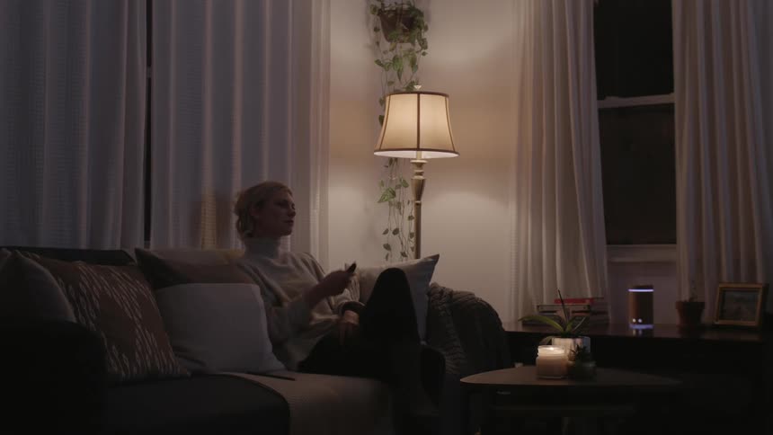 A woman picks up the remote and leans back on her couch as she turns on the television