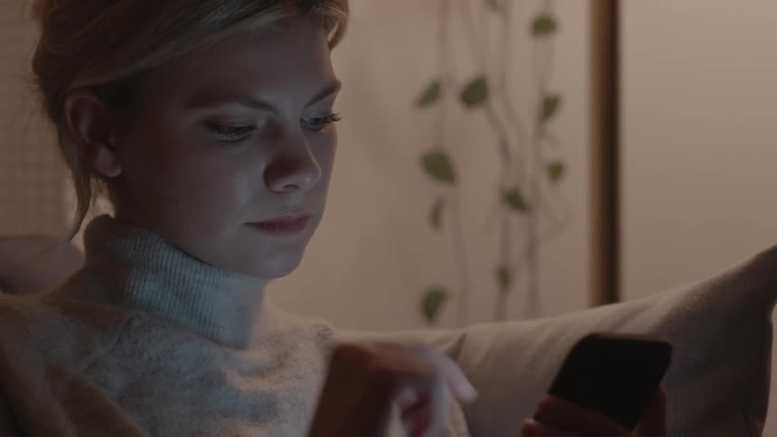 Woman scrolling through social media on her cell phone in living room