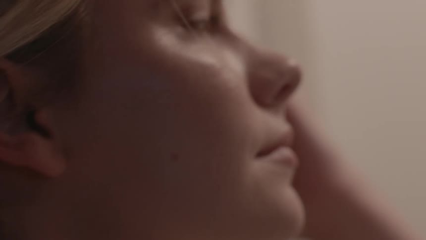 A young woman with her hand against her face looks around