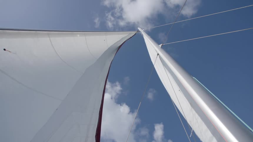 Wind blows through the sails of a sailboat with clouds floating overhead