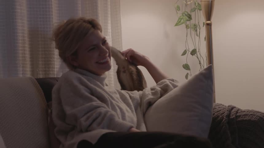 Woman on sofa pets cat and smiles