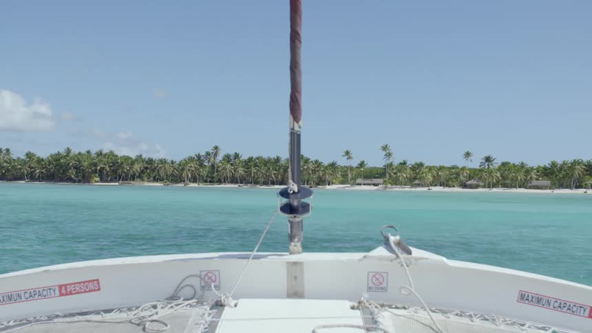 A boat on the bluegreen waters of the ocean near a beach covered in palm trees