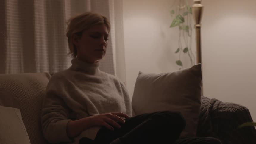 A woman sits on the couch and looks at her cell phone