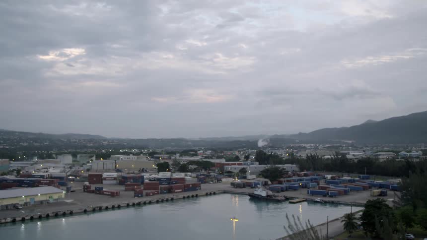 Warehouse surrounded by freight containers borders water as mist covers mountains