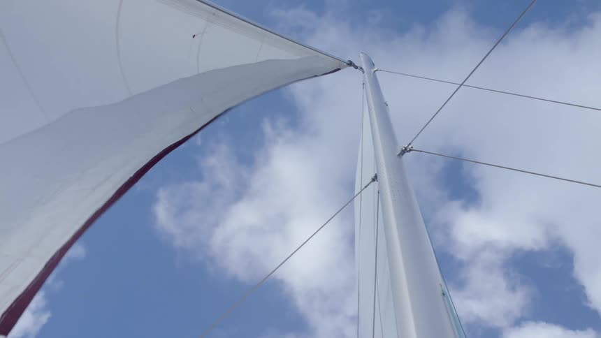A sail on a sailboat flapping in the wind with the sky up above
