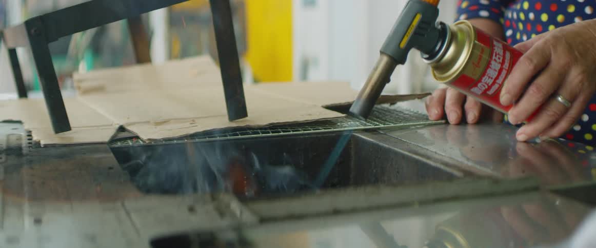 A man uses a butane torch on a piece of metal outdoors