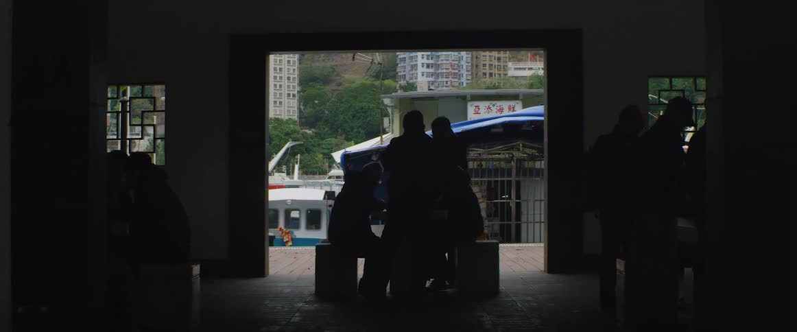 Crowd of people sit inside a dark building while the breeze blows a tarped roof outdoors