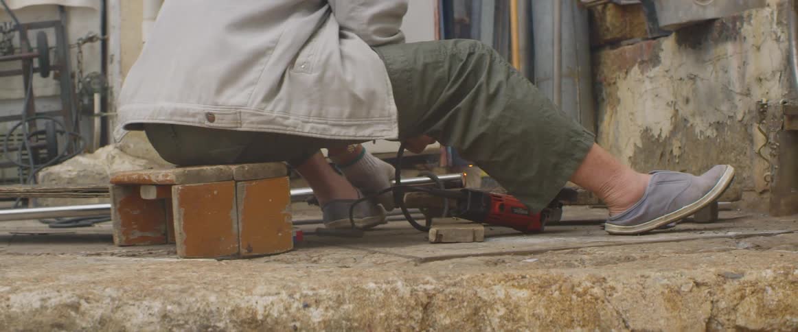 Sparks fly as a woman welds metal on a sidewalk outdoors