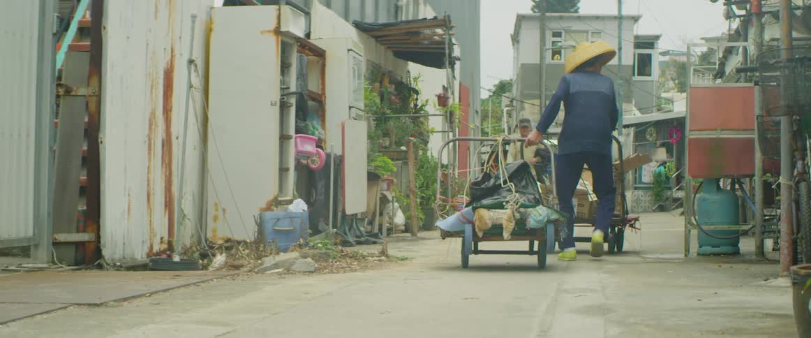 A man pulls a cart behind him walking through a village alley