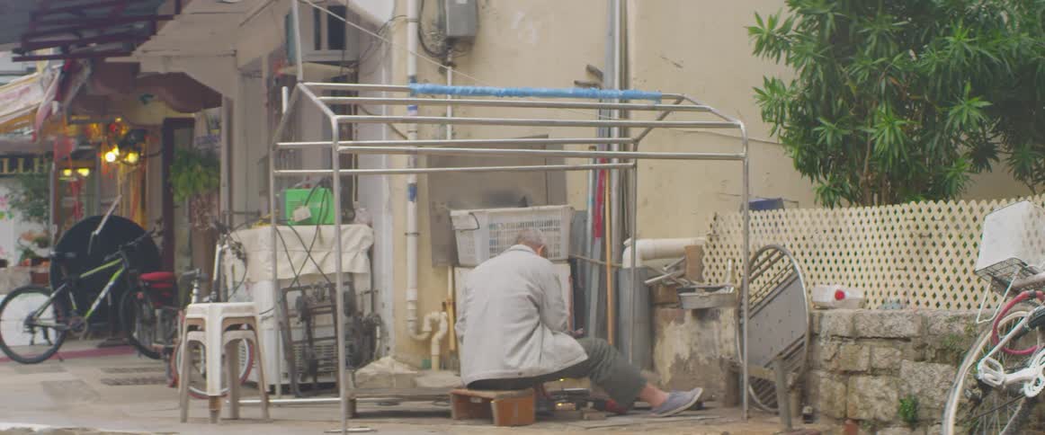 A man sits on short bench outside making repairs and causing sparks and light flashes