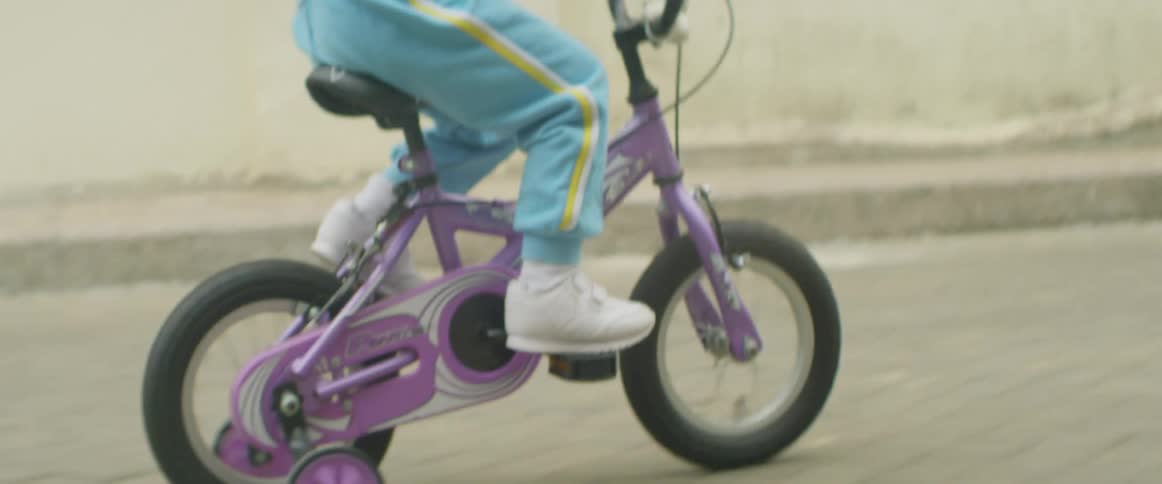 A young child rides a purple bicycle with training wheels