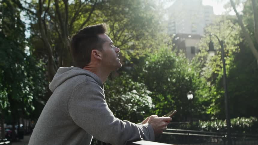 Man reclined on a fence in a park uses smartphone