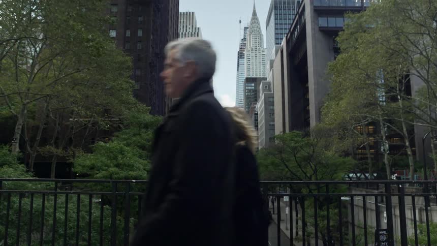 A man and woman walk over a pedestrian bridge above a city street