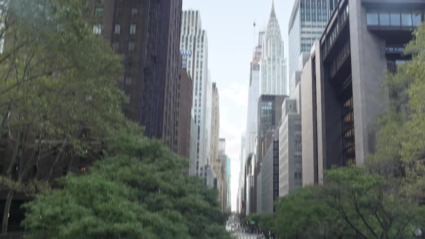 People stand on a city sidewalk as taxis and cars drive by