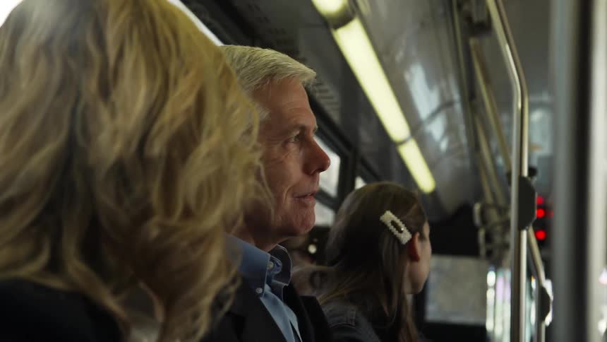 A blonde woman nods her head as the man beside her on the train talks with her